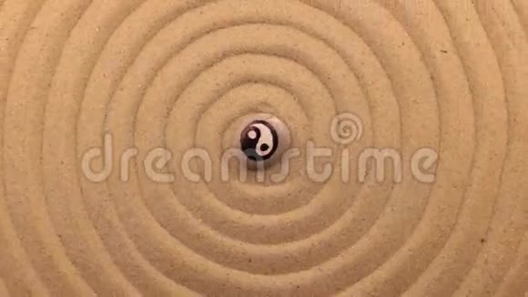 旋转一块白色的石头上面有一个阴阳标志躺在一个由沙子制成的螺旋中心视频的预览图