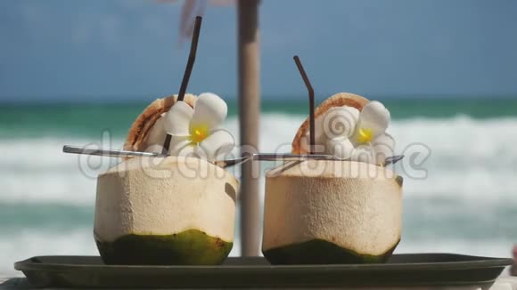热带新鲜椰子鸡尾酒在海滩咖啡馆装饰梅花有绿松石海背景3840x2160视频的预览图
