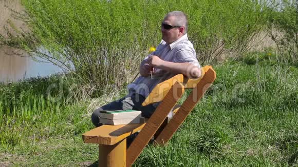 带蒲公英的人在河边的长椅上放松视频的预览图