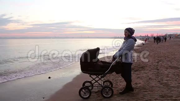 年轻的母亲带着一个孩子晚上在海边散步视频的预览图