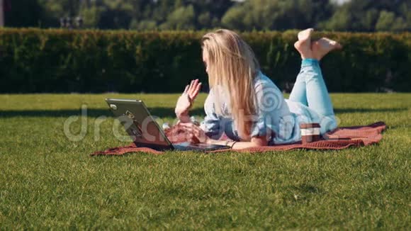 一个年轻女人用笔记本电脑躺在草坪上视频的预览图