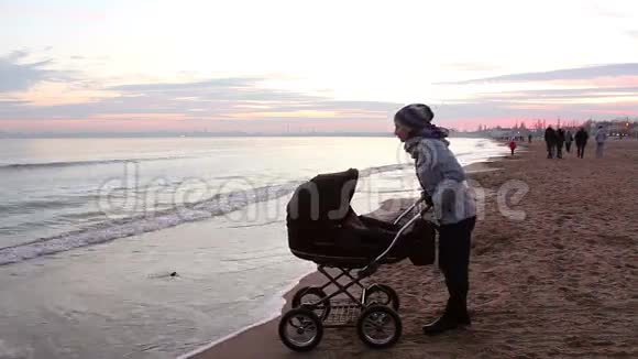年轻的母亲带着一个孩子晚上在海边散步视频的预览图