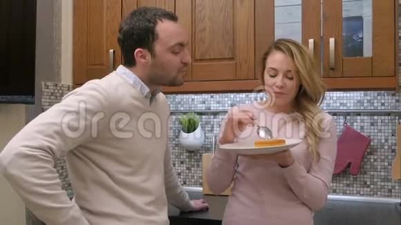 饥饿的夫妇吃着美味的蛋糕女人喂男人在家里的厨房里视频的预览图