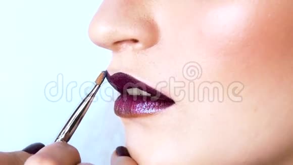 化妆师正在用刷子在模特的嘴唇上涂上明亮的紫色的小锡她的嘴微微张开快关门视频的预览图