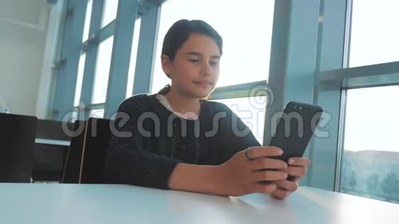十几岁的女孩正在聊天生活方式在一张桌子阳光下的咖啡馆里在智能手机里的信使里交流视频的预览图