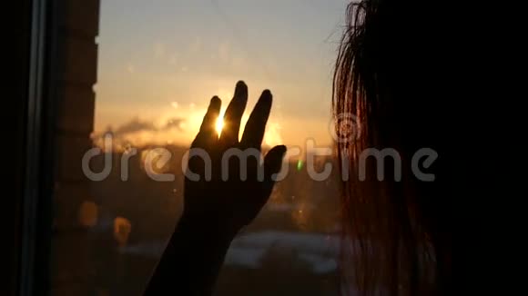 年轻女子通过窗户欣赏日落试图用手触摸太阳玩眩光1920x1080视频的预览图