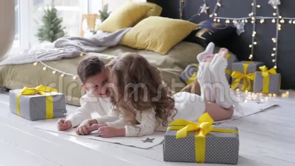 孩子们躺在圣诞节室内的背景上在礼物旁边的男孩和女孩视频的预览图