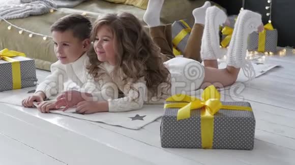 孩子们躺在圣诞节室内的背景上在礼物旁边的男孩和女孩视频的预览图