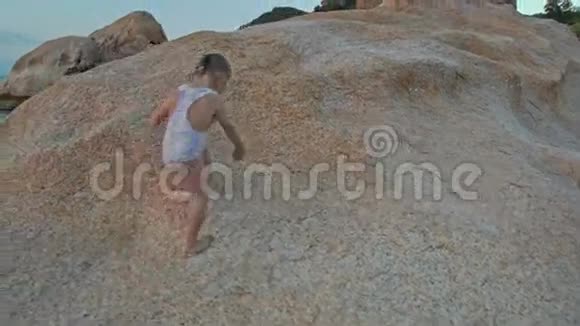 在海滩日落时特写小女孩爬上大型裸岩视频的预览图