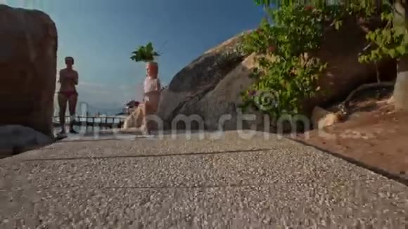 小女孩从母亲那里沿着海滩上的落基小径奔跑视频的预览图