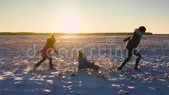 十几岁的女儿和母亲拉着小儿子在雪橇上跑剪影一家人在冬天玩积极健康视频的预览图