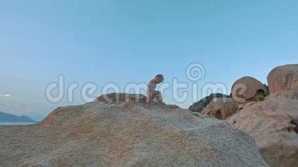 小女孩在海滩日落时的大裸岩顶上视频的预览图