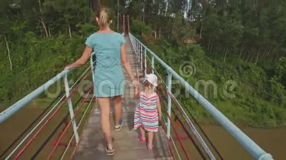 母亲手牵着小女孩沿着河上的桥视频的预览图