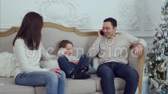 可爱的小男孩坐在沙发上模仿他父亲在打电话视频的预览图