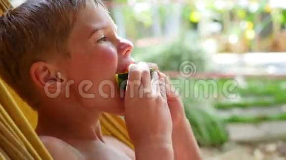在炎热的夏日里孩子躺在吊床上吃着香甜多汁的西瓜视频的预览图
