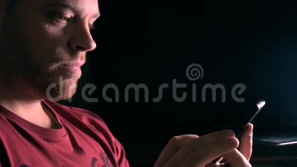 一个英俊的小胡子男人在黑暗的房间里用他的手机视频的预览图
