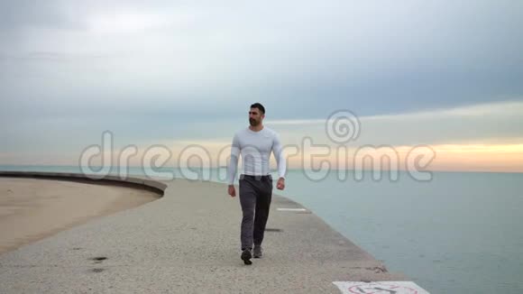 男跑者正沿着美丽的海滨散步一边用耳机听音乐准备好锻炼了视频的预览图