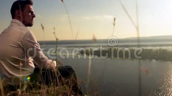 年轻的帅哥坐在山顶上看风景视频的预览图