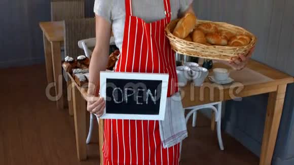 女面包师拿着小面包和开放式招牌的肖像视频的预览图