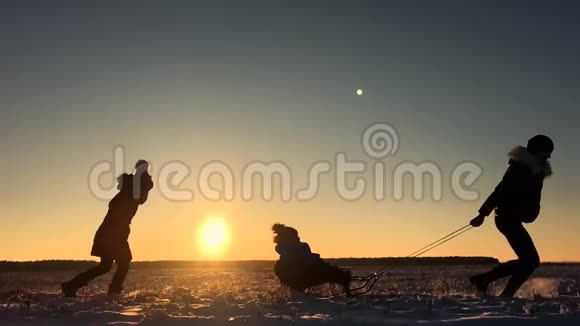 十几岁的女儿和母亲拉着小儿子在雪橇上跑剪影一家人在冬天玩积极健康视频的预览图