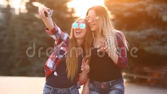 一幅快乐的两个微笑的女孩在智能手机上自拍照片的肖像城市背景黄昏的日落笼罩着视频的预览图