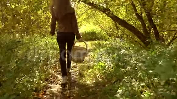 一个穿着棕色夹克的女孩背着篮子走过秋天森林的慢动作稳定录像视频的预览图