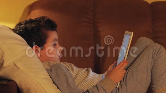 侧视图一个小男孩躺在床上在家看平板电脑视频的预览图