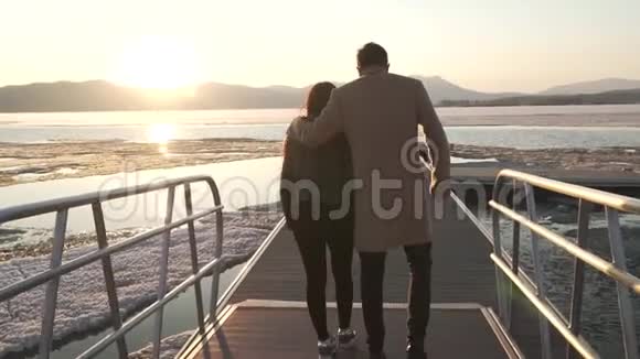 冰冻但幸福的一对情侣在码头漫步日落股票录像视频的预览图