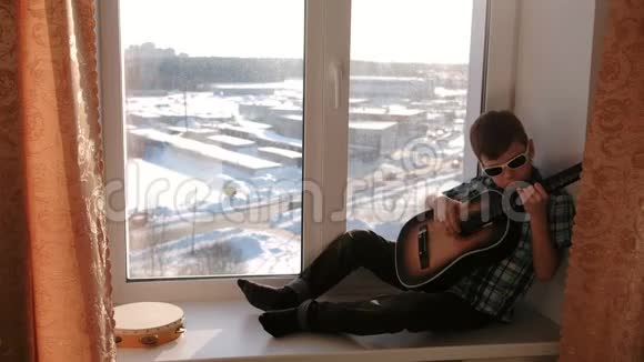 演奏乐器戴太阳镜的男孩坐在窗台上弹吉他视频的预览图