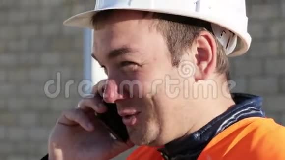 戴着头盔和背心的白人男子在户外工作场所用电话微笑交谈视频的预览图