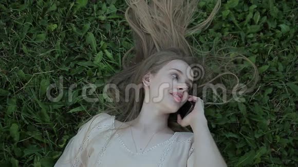 坐在草地上打电话的年轻女子视频的预览图