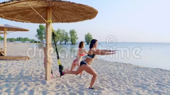 两名身穿泳衣的年轻女性教练用健身TRX系统做运动TRX吊带视频的预览图