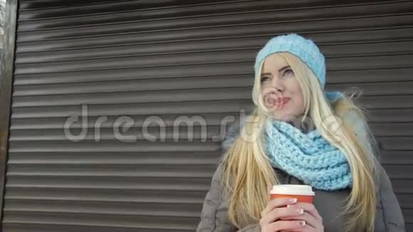 漂亮的年轻女人拿着一杯咖啡在墙的背景上暖手视频的预览图