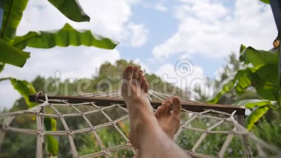 在阳光明媚的日子里一个人光着脚在吊床上休息视频的预览图