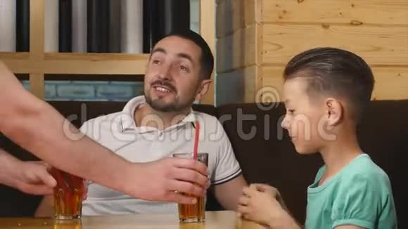 父亲和小儿子坐在咖啡馆里喝着果汁视频的预览图