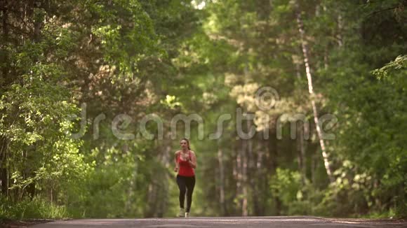 年轻女子在夏天的森林里慢跑这个女孩去买运动无线耳机有运动服的运动员慢慢慢慢视频的预览图