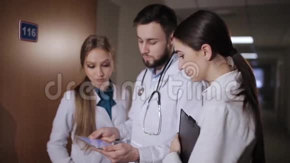 医生在医院走廊实习生解释说病人接受医生和两个女实习生分析诊断视频的预览图