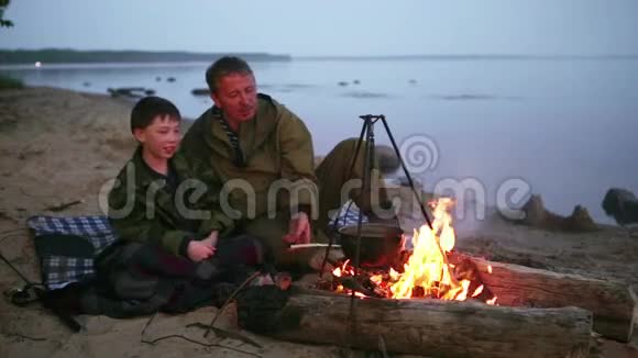父子俩围坐在湖边的篝火旁视频的预览图
