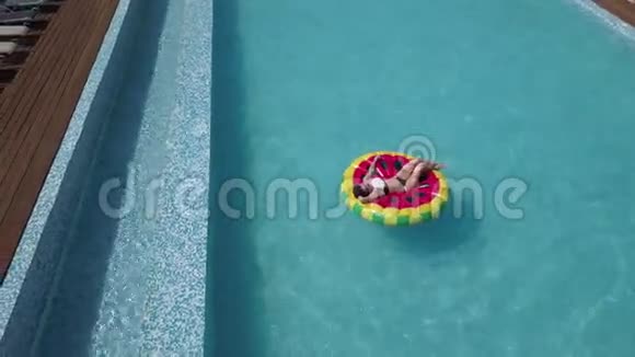 空中年轻女子放松在充气西瓜床垫在水晶清澈的游泳池女孩在晒太阳视频的预览图
