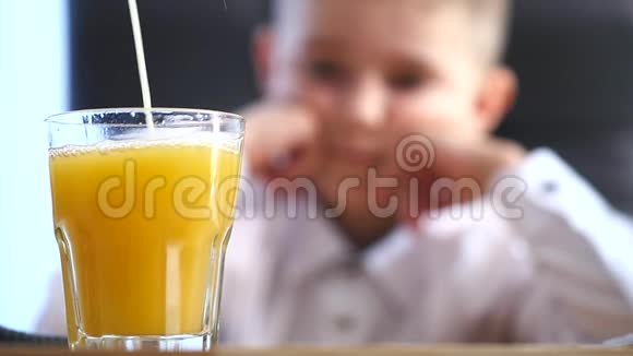 橙汁倒进玻璃杯里小男孩的背景选择性聚焦视频的预览图