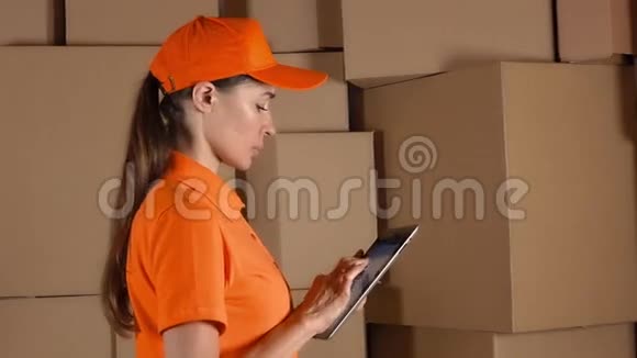 穿着橙色制服的女孩计数储存箱并使用她的平板电脑与棕色纸箱背面现代商业视频的预览图