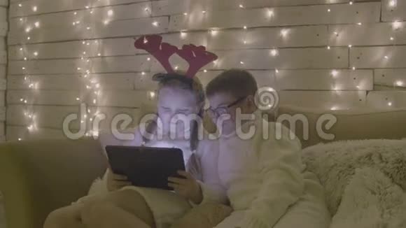 微笑的小女孩和男孩与平板电脑电脑坐在沙发上的背景圣诞装饰视频的预览图