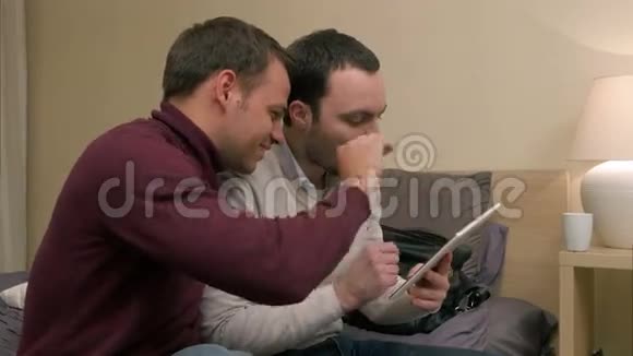 年轻的男性朋友坐在沙发上用平板电脑摆弄着什么笑着视频的预览图
