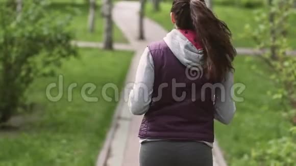 跑步女孩一位年轻的运动员穿过夏季公园从后面看摄像机跟随模型慢慢视频的预览图