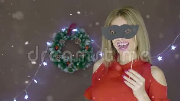 在圣诞节背景下穿着红色裙子配香槟笛和面具的金发女士视频的预览图