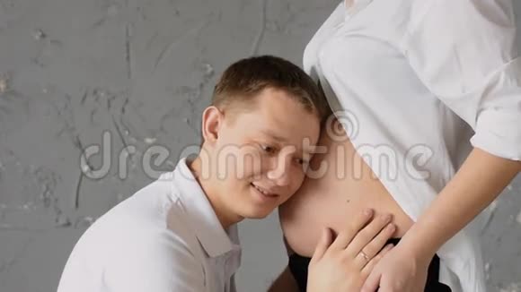 照顾幸福的年轻人亲吻他怀孕的妻子的腹部慢动作视频的预览图