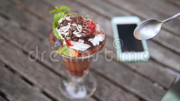 女性在木制老式餐桌上用手机在咖啡厅吃健康的冰淇淋甜点4K慢动作视频的预览图