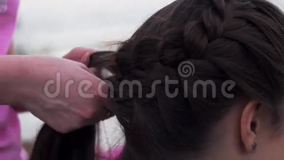 穿着粉红色衬衫的女人编织辫子给年轻的黑发女孩发型时尚视频的预览图