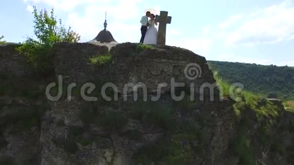 站在悬崖上接吻的新婚夫妇的鸟瞰图视频的预览图