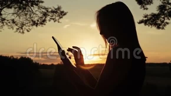 日落时分在森林中使用数字平板电脑的女性剪影视频的预览图